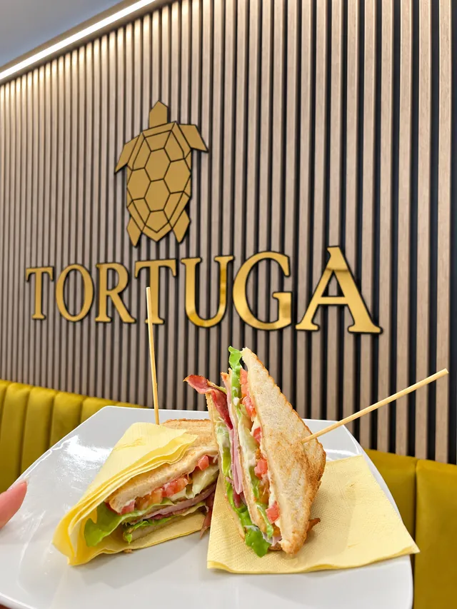 Club sandwich servito davanti all'insegna dorata Tortuga, su una parete a listelli di legno